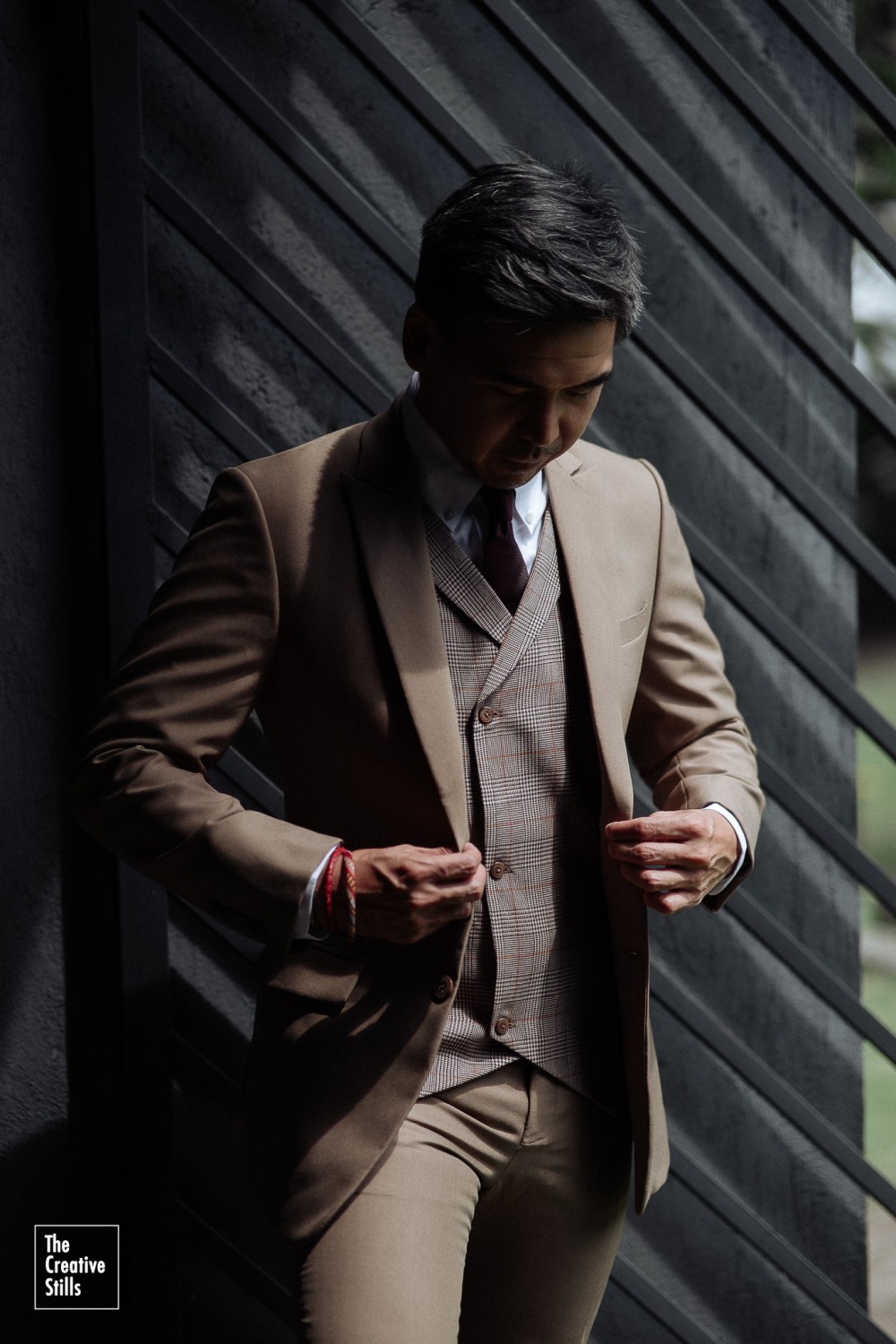 Мужчина в строгом серо-коричневом костюме с клетчатым жилетом и бордовым галстуком